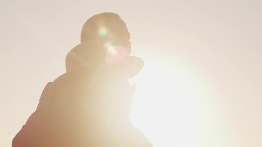 A man hugging a woman with a hat with the sky and the sun in the background