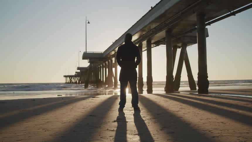 A man stands on the beach looking out at the ocean just after sunrise