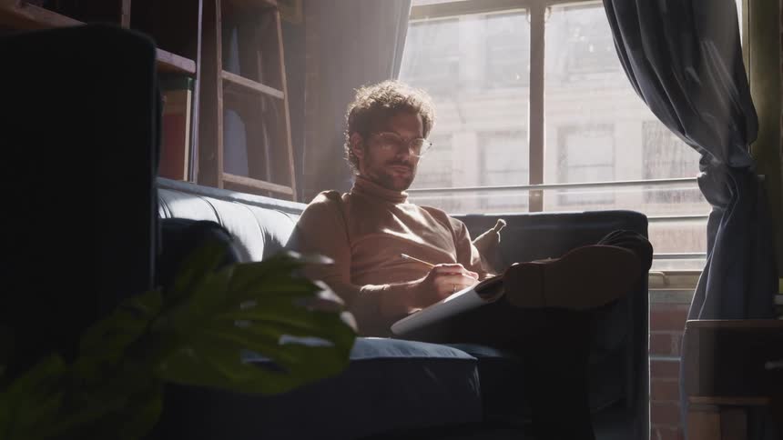 A man sits quietly in a home study with a pen and notebook