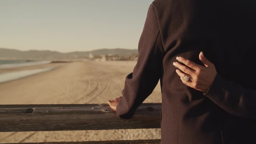 A woman rubs her husbands back as they stand on a bridge on the beach