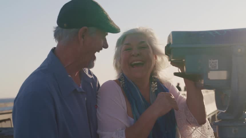 An elderly couple laugh together while looking through a viewfinder