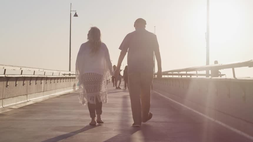 Elderly couple walk on a pier holding hands at sunset