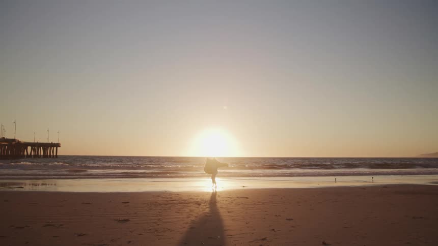 Woman running and turning around happily on the beach is silhouetted against the sunset