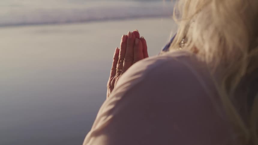 A woman standing outdoors has her hands together as if she is praying
