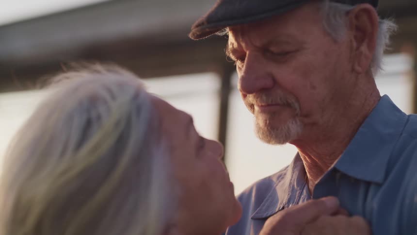 An elderly woman looks up at her husband as they slow dance outside
