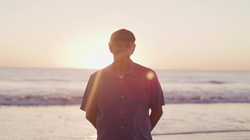 The sun hangs low in the sky behind a man standing on the beach