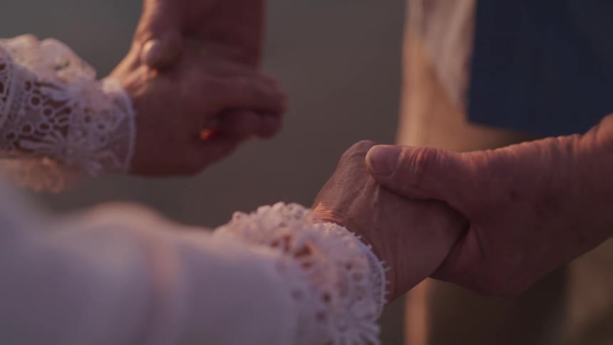 An elderly couple holding hands outside on a breezy day