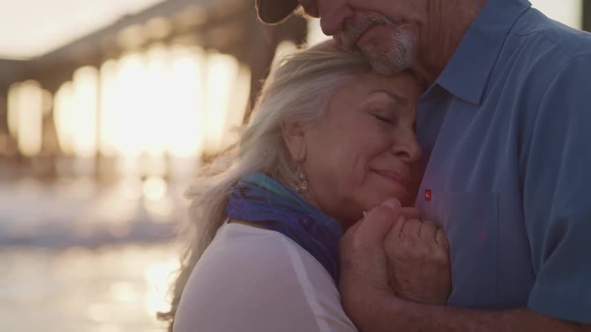 An elderly couple outside holding and hugging each other