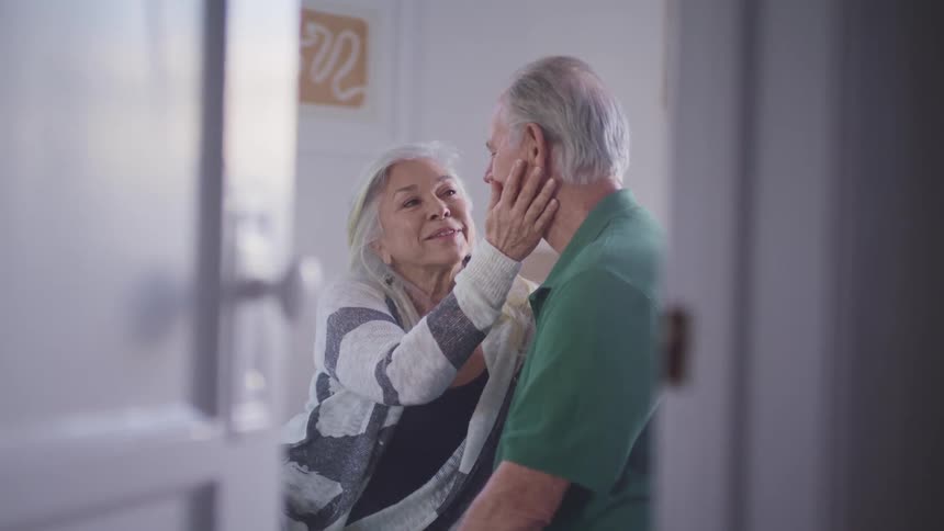 An elderly woman caresses her husband face at home