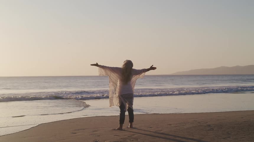 A woman is stretching by the coast of a beach