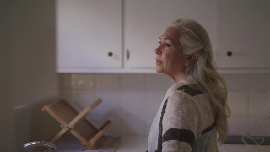 An elderly female standing in a kitchen smiling