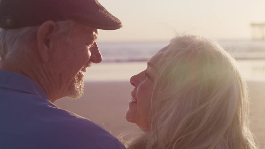 An older man and woman kiss and hug standing on a quiet beach
