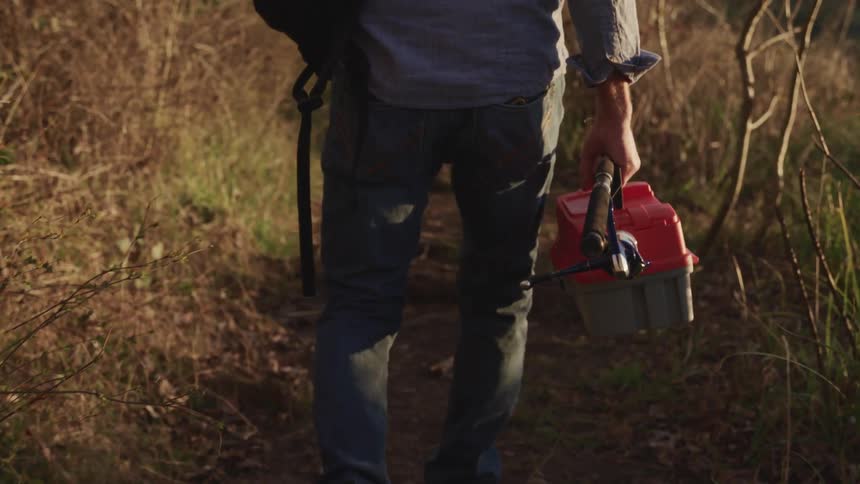 A man walking down a path carrying fishing gear