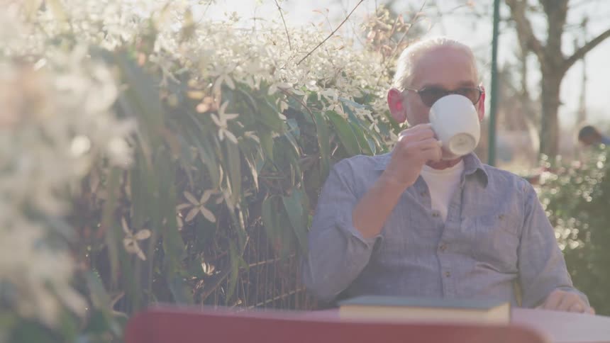 An elderly man sits outside and drinks coffee