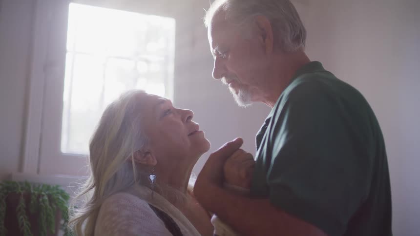 An elderly couple stand close together while gazing into each others eyes