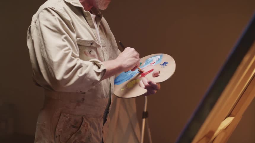 A man mixes paint on a palette with his paint brush