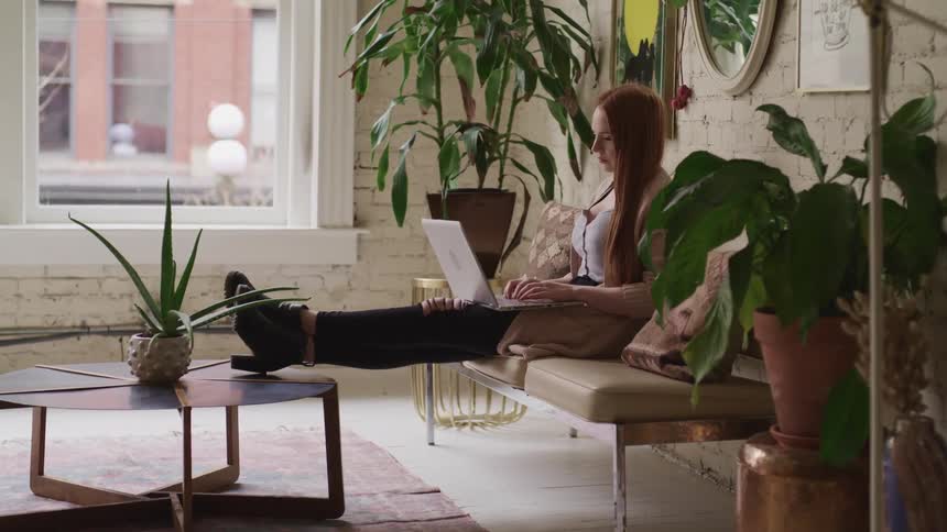 A woman is sitting indoors and browsing on a laptop