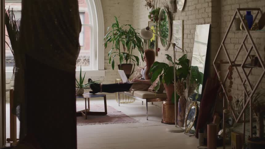 A woman types on her laptop while sitting in the living room of her heavily decorated apartment
