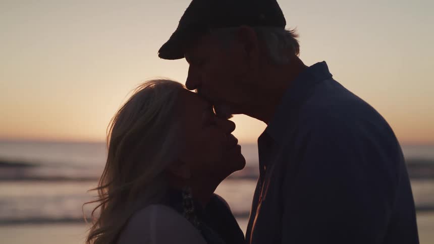 A man kisses the forehead of a woman while they stand closely on the beach