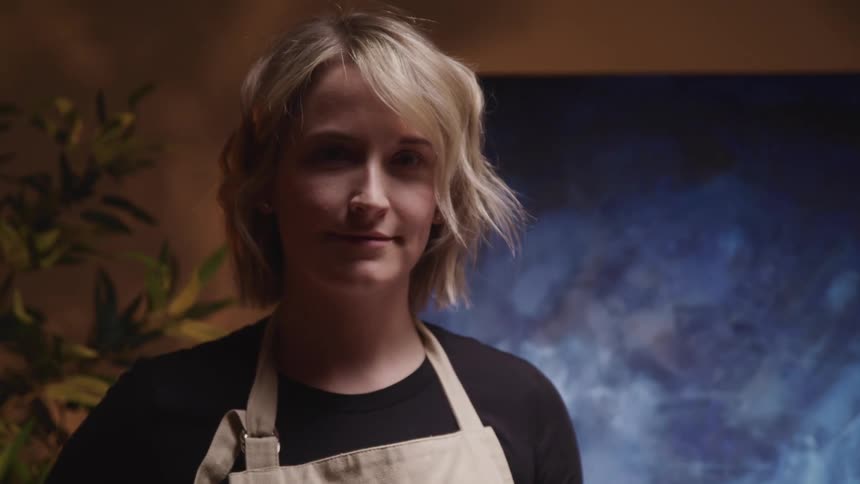 Blonde female painter with a brown apron stands by the oil painting