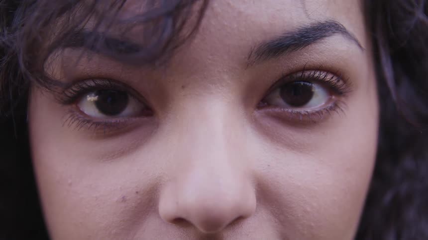A young woman with dark hair and well manicured eyebrows stares forward without blinking