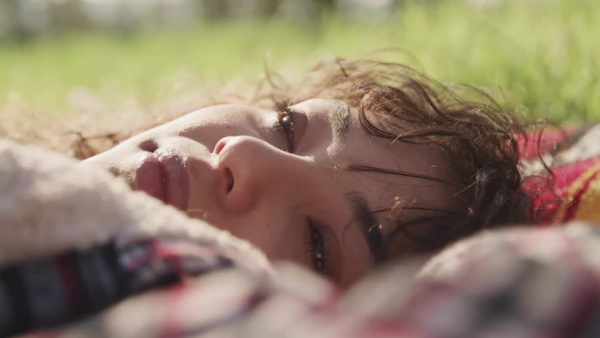 Young woman laying on a blanket over the grass is falling asleep