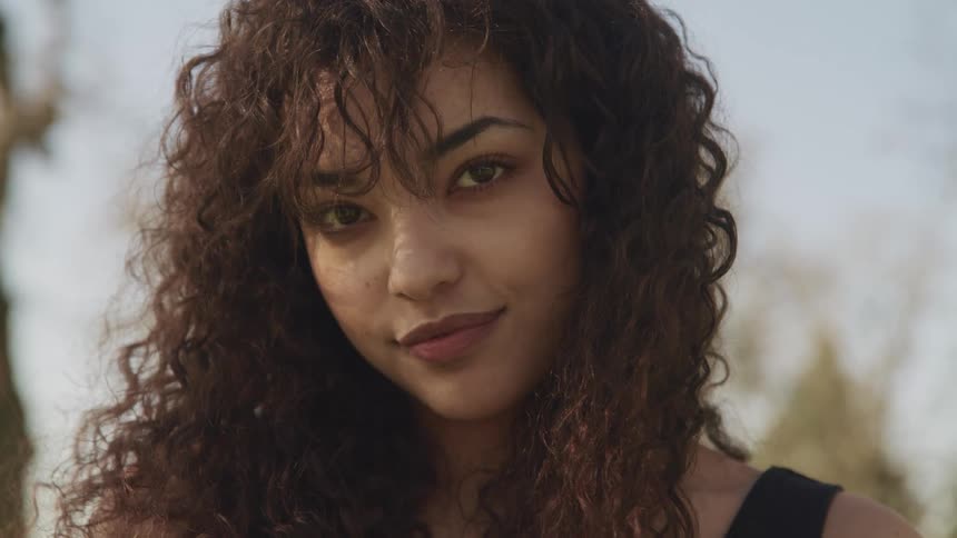 A woman with long and dark curly hair poses and smiles