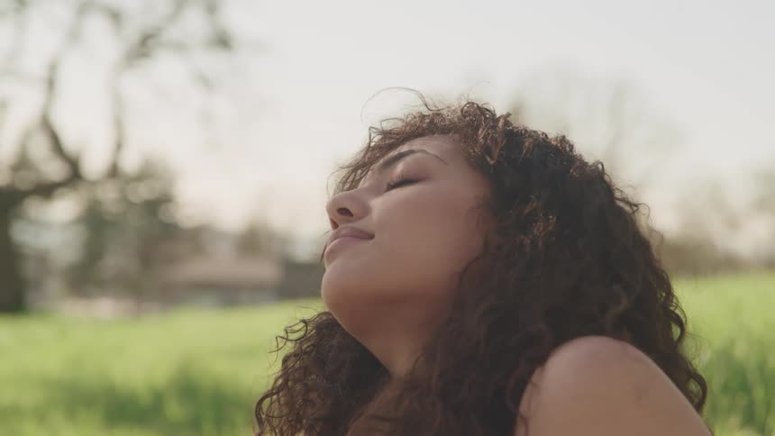 A teenage girl closes her eyes as she sits in a grassy field