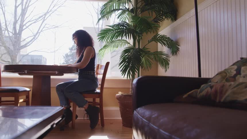 Woman sits at a table next to a window
