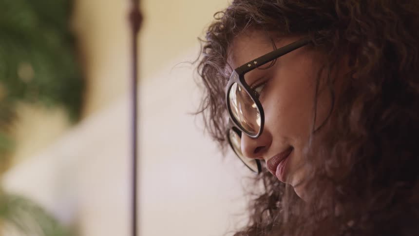 Woman with glasses and brown curly hair looks down and smiles slightly