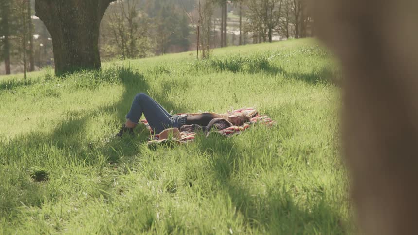 Woman with jeans and boots lies on a rug on green grass hill slope