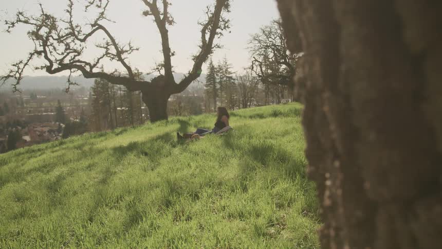 Woman with jeans and boots sits on a rug on green grass hill slope
