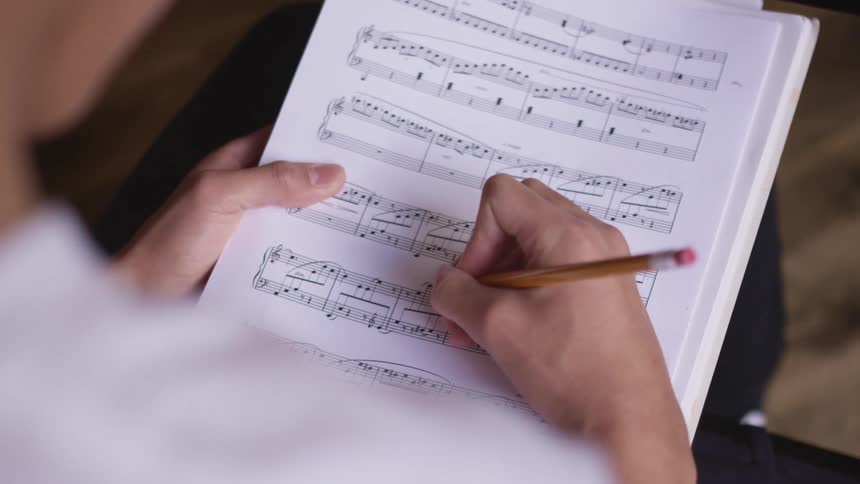 A young person writes out the musical notes for a song on a sheet of paper
