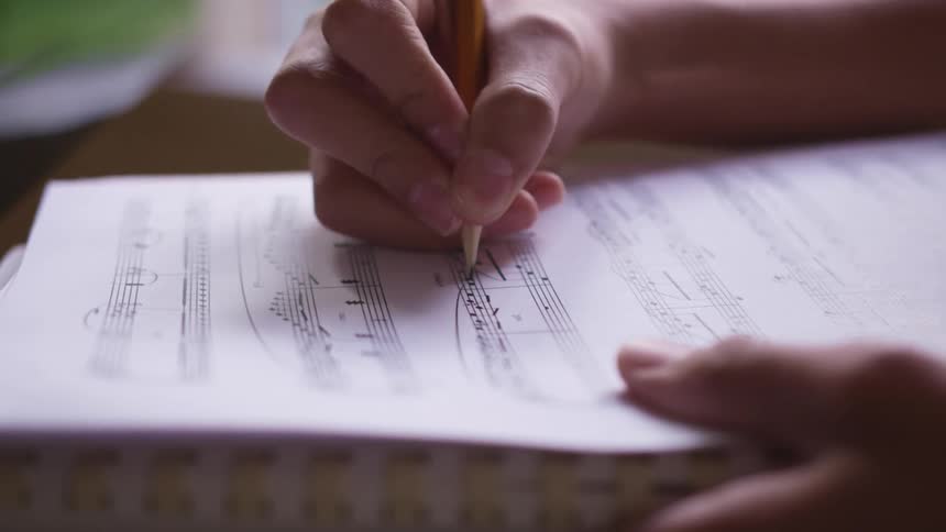 A person is holding a pencil and drawing musical notes on a treble clef
