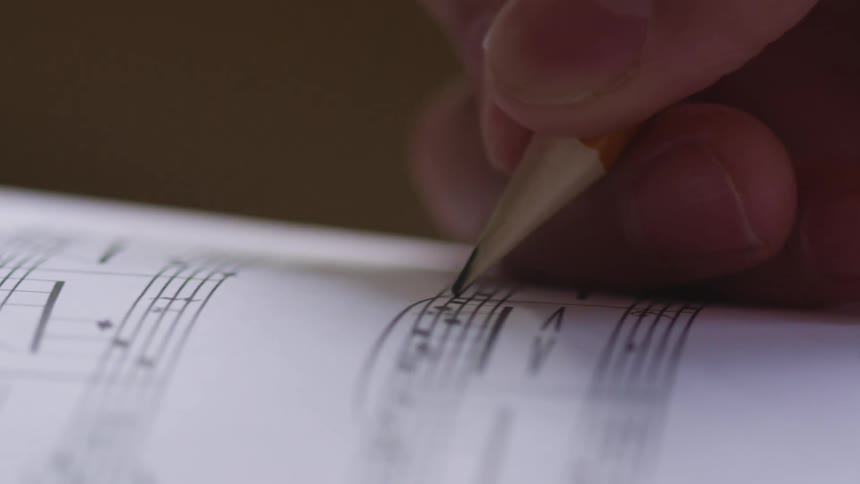 A musician draws notes on a piece of sheet music
