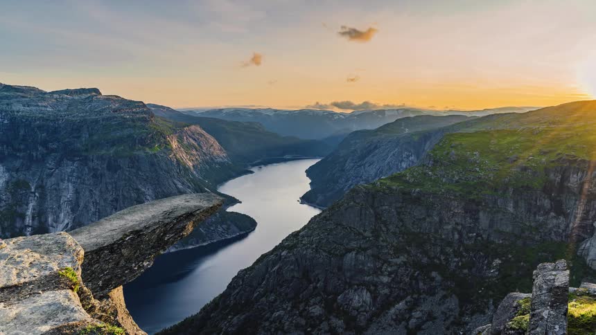 A river surrounded by cliffs with the mountain range the sky and clouds in the background