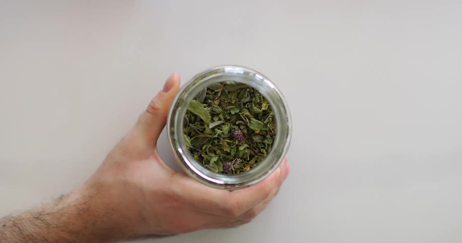 A man opens a jar of herbs on a white table