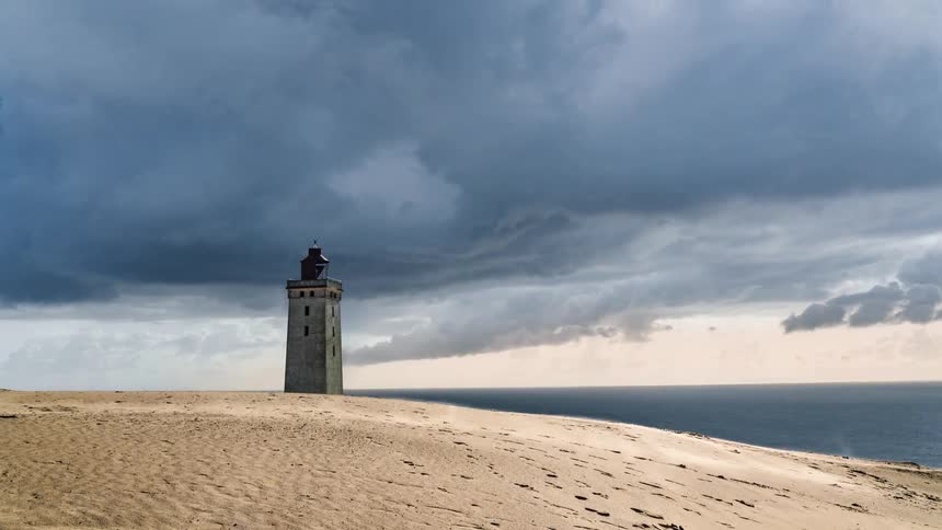 Time lapse of people walking past a tower on a beach as dark storm clouds pass over