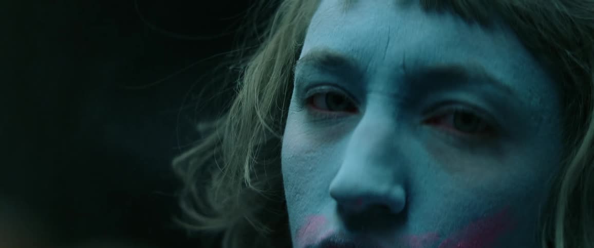 A woman with blue and pink makeup on her face looking up and staring