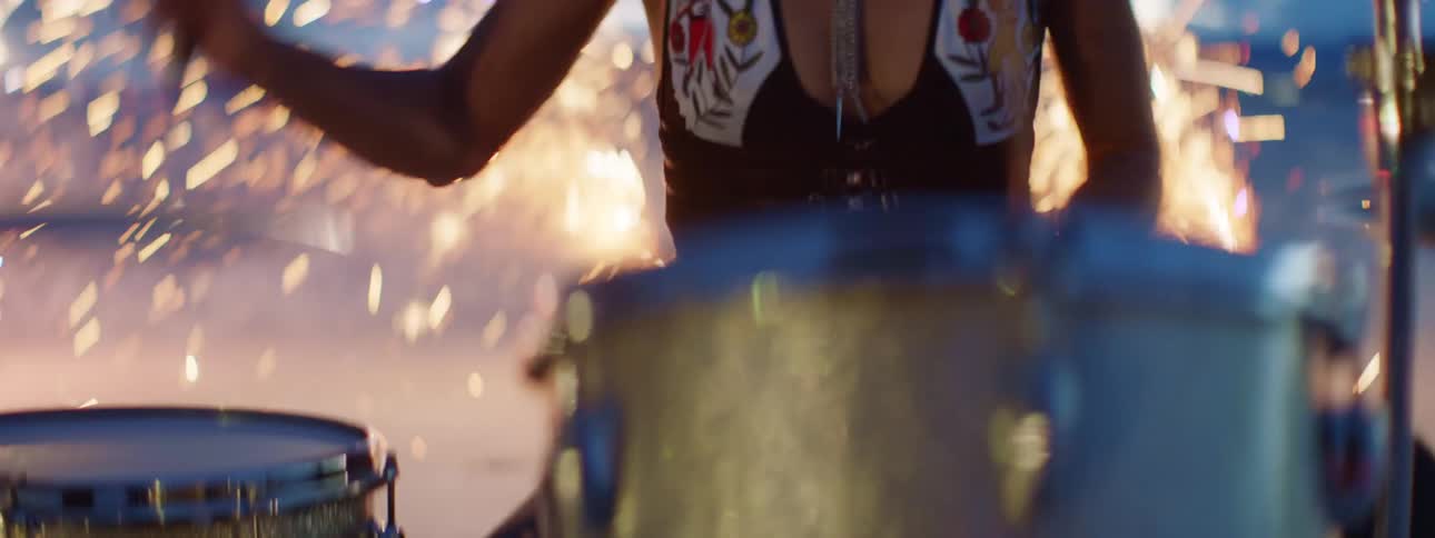 Female drummer performs an aggressive drum set on stage in front of fireworks outdoors at sunset