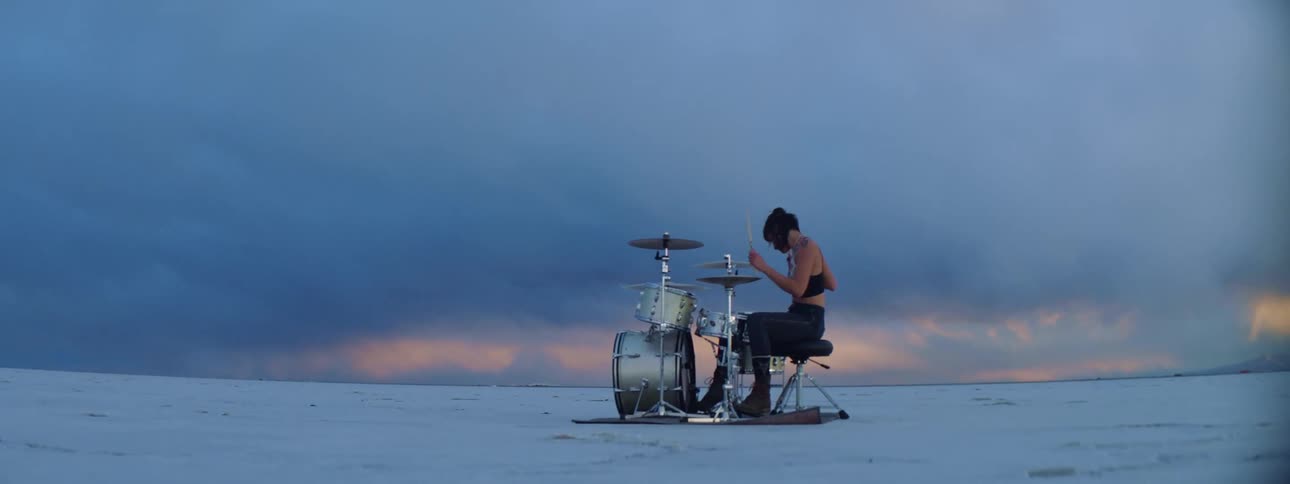 A female sitting outside playing the drums