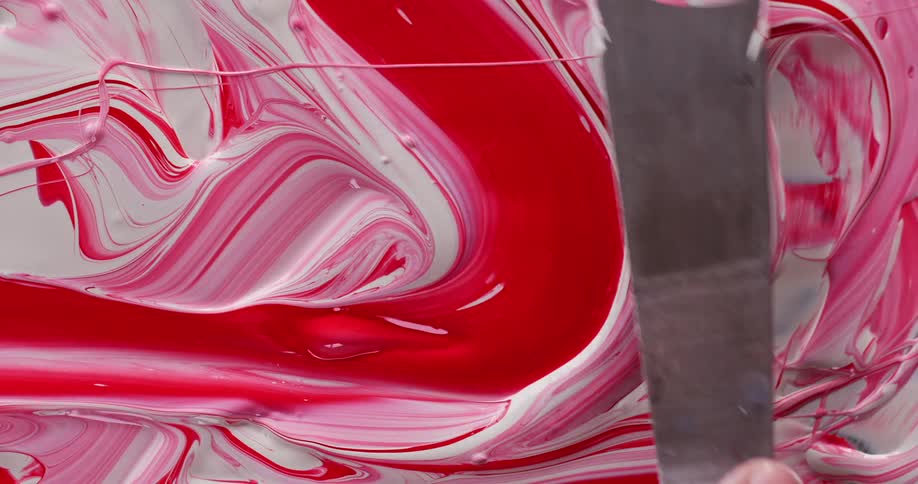 A person uses a painting knife to mix red and white paint