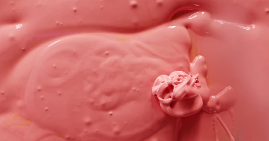 Pink paint drips from a painting knife onto a pool of pink paint before the knife is used to smooth it