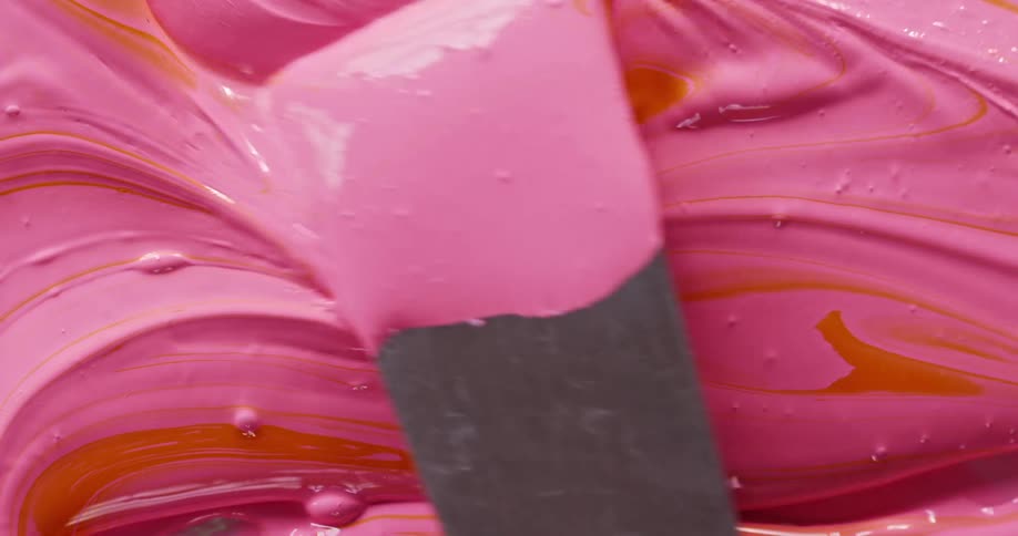 Pink and orange paints are mixed with a palette knife