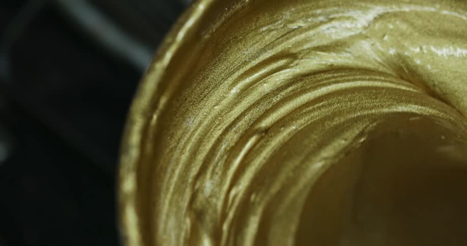 A pot of gold paint being mixed with a palette knife
