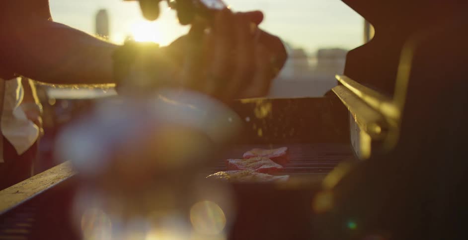 Seasoning steaks on grill at sunset with skyline in the background