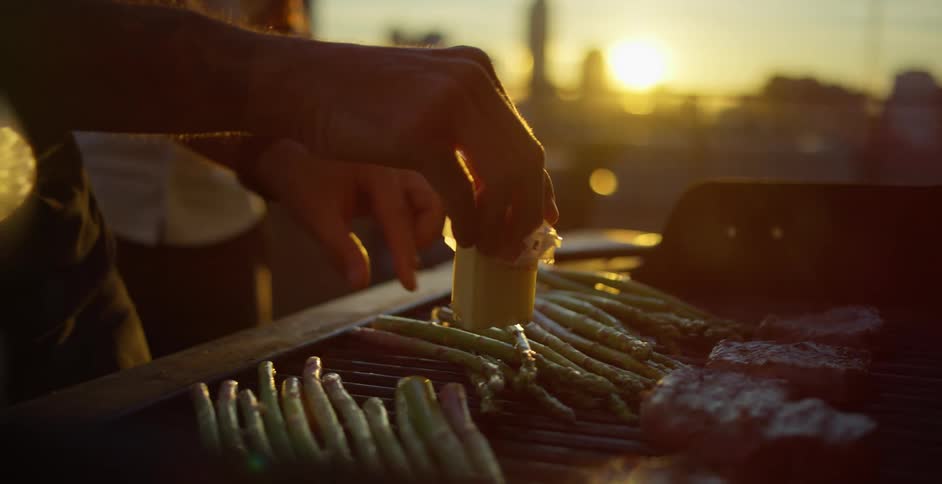 A person places butter on vegetables on a roof top grill