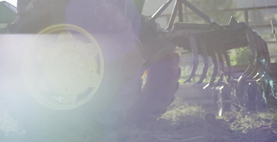 A tractor with an attached rake drives through a field