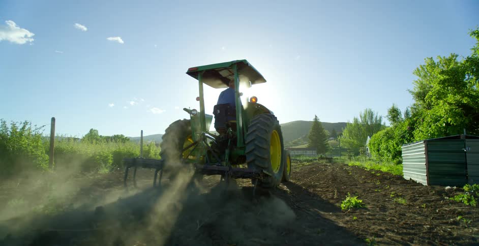 A farmer drives a tractor over soil in a rural field on a sunny day