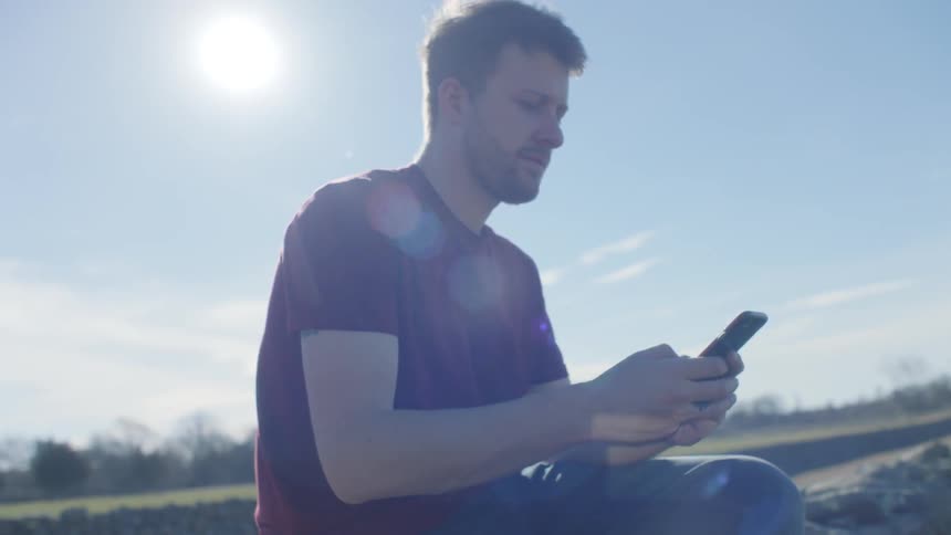 A man is sitting outside using a phone